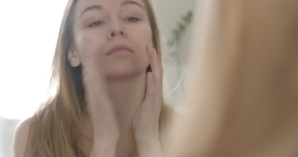 Young woman is touching her face at the mirror — Stock Video