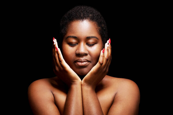 The portrait of black woman touching face with hands on black background.