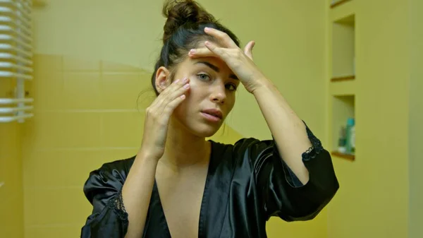 Eine junge Frau blickt in den Spiegel und überprüft ihre ersten Falten — Stockfoto