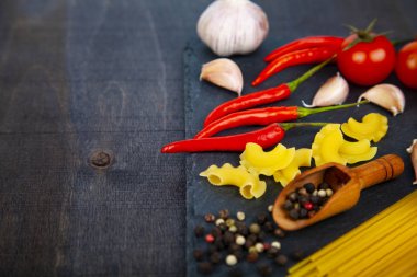 Karanlık bir arka plan üzerinde farklı makarna. Pişmemiş makarna, biber, domates ve fesleğen yakın çekim.