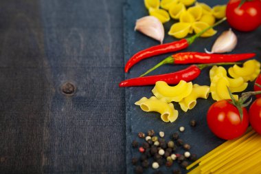 Karanlık bir arka plan üzerinde farklı makarna. Pişmemiş makarna, biber, domates ve fesleğen yakın çekim.