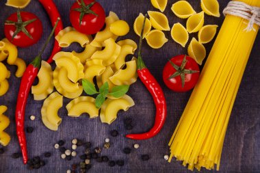 Koyu ahşap arka plan üzerinde farklı makarna. Pişmemiş makarna, biber, domates ve fesleğen yakın çekim.