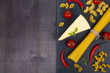 Farklı makarna ve peynir koyu ahşap arka plan üzerinde. Pişmemiş makarna, biber, domates ve fesleğen yakın çekim.