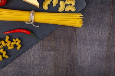 Farklı makarna ve peynir koyu ahşap arka plan üzerinde. Pişmemiş makarna, biber, domates ve fesleğen yakın çekim.