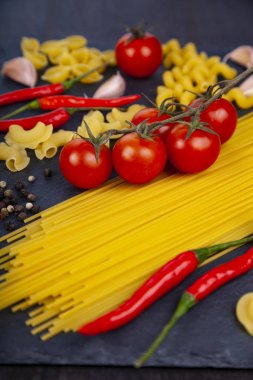 Ahşap arka plan üzerinde farklı makarna. Pişmemiş makarna, biber, domates ve fesleğen yakın çekim.