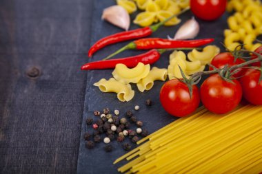 Ahşap arka plan üzerinde farklı makarna. Pişmemiş makarna, biber, domates ve fesleğen yakın çekim.