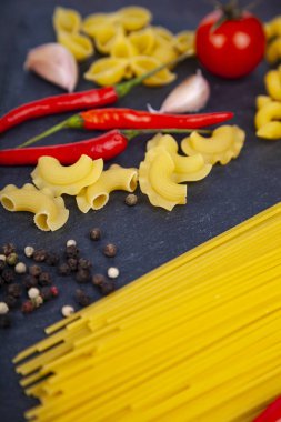 Ahşap arka plan üzerinde farklı makarna. Pişmemiş makarna, biber, domates ve fesleğen yakın çekim.