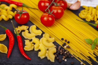 Ahşap arka plan üzerinde farklı makarna. Pişmemiş makarna, biber, domates ve fesleğen yakın çekim.