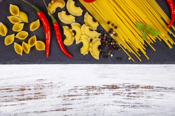 Different pasta on a  wooden background. Raw pasta, chili, tomatoes and basil close-up.