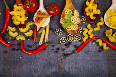 Kaşık koyu ahşap arka plan, üstten görünüm üzerinde farklı makarna. Pişmemiş makarna, biber, domates ve fesleğen yakın çekim.