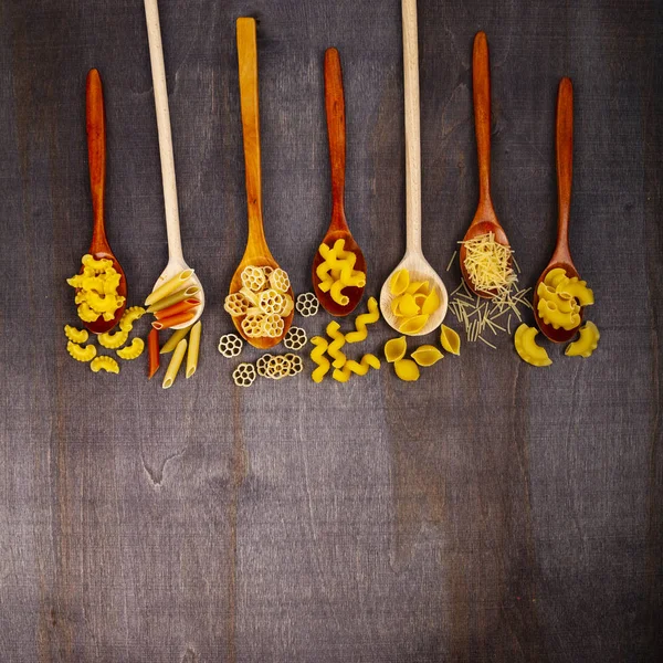 不同的面食在勺子上的黑木背景 顶部的看法 生面食 西红柿和罗勒特写 — 图库照片