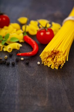 Koyu ahşap arka plan üzerinde farklı makarna. Pişmemiş makarna, biber, domates ve fesleğen yakın çekim.