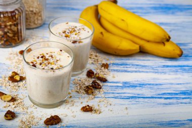 Smoothies ile mavi ahşap bir masa üzerinde bir muz, ceviz ve yulaf gevreği. Lezzetli tatlı.