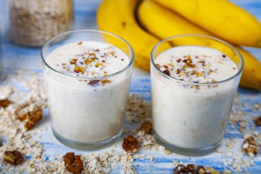 Smoothies ile mavi ahşap bir masa üzerinde bir muz, ceviz ve yulaf gevreği. Lezzetli tatlı.