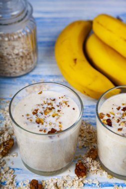 Smoothies ile mavi ahşap bir masa üzerinde bir muz, ceviz ve yulaf gevreği. Lezzetli tatlı.