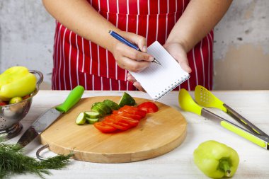 Bir defter mutfakta bir kırmızı önlük kadın yazar. Yemek için tarifi