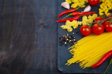 Ahşap arka plan üzerinde farklı makarna. Pişmemiş makarna, biber, domates ve fesleğen yakın çekim.