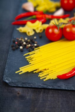 Ahşap arka plan üzerinde farklı makarna. Pişmemiş makarna, biber, domates ve fesleğen yakın çekim.