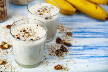 Smoothies ile mavi ahşap bir masa üzerinde bir muz, ceviz ve yulaf gevreği. Lezzetli tatlı.