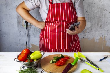 Bir kırmızı önlük kadın mutfakta telefon ile.