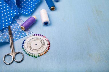 Mavi ahşap arka plan üzerinde dikiş aksesuarları. Mavi kumaş, makas ve iş parçacığı.