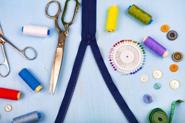 Bunca fermuar ve dikiş aksesuarları mavi ahşap arka plan üzerinde. Teyp, iğne, düğme, fermuar, makas ve iş parçacığı ölçme.