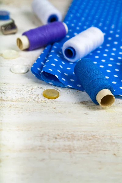 Sewing accessories and blue fabric on a  wooden background. Fabrics, measuring tape, pins, buttons and thread.