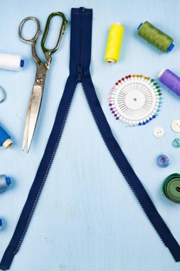 Bunca fermuar ve dikiş aksesuarları mavi ahşap arka plan üzerinde. Teyp, iğne, düğme, fermuar, makas ve iş parçacığı ölçme.