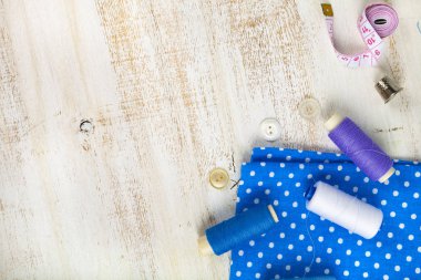 Dikiş aksesuarları ve ahşap bir zemin üzerine mavi kumaş. Kumaşlar, teyp, iğne, düğmeler ve iş parçacığı ölçme.