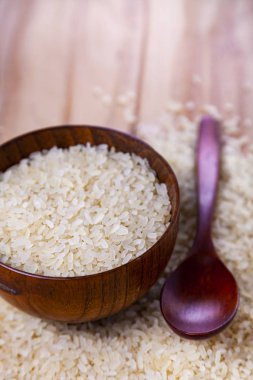 Uzun taneli pirinç bir kase ve kaşık bir ahşap arka plan üzerinde biraz uzun tuttum. Sağlıklı bir diyet için madde.