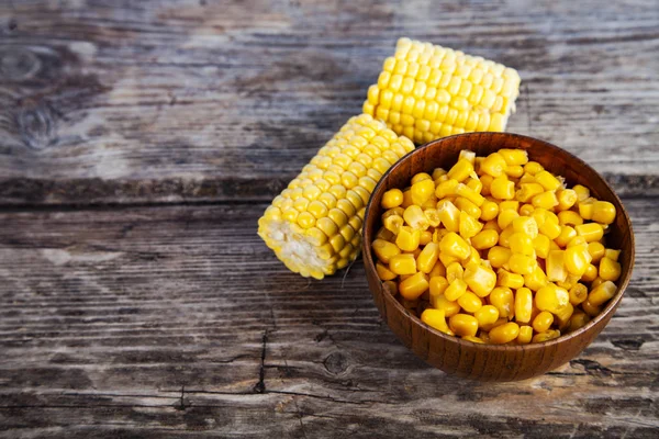 Raw corn and canned corn in a bowl on an old wooden table.