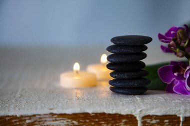 Spa uygulamaları ahşap masa üzerinde. Deniz tuzu, spa taşları, orkide ve yanan mumlar.