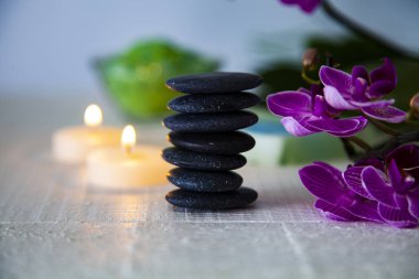 Spa uygulamaları ahşap masa üzerinde. Deniz tuzu, spa taşları, orkide ve yanan mumlar.