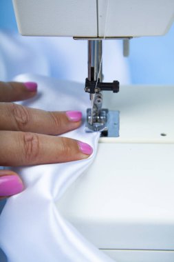 Kadın bir dikiş makinesi diker. Dikiş makinesi ve beyaz saten kumaş yakın çekim
