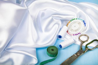 Mavi ahşap arka plan üzerinde dikiş aksesuarları. Beyaz saten kumaş, makas ve iş parçacığı.