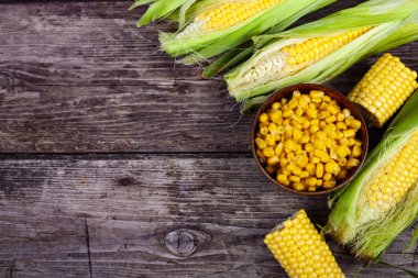 Olgun sarı Mısır ve ahşap bir masa üzerinde bir ahşap kase konserve mısır. Sarı olgun Mısır, üstten görünüm