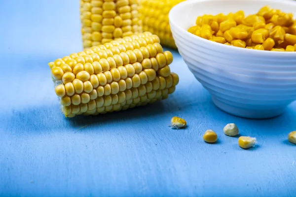 Ripe corn on a blue table close-up. Raw and canned corn in a white bowl.