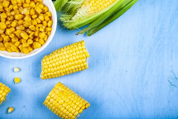 Ripe corn on a blue table close-up. Raw and canned corn in a white bowl, top view.