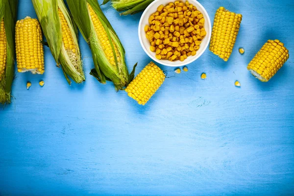 Ripe corn on a blue table close-up. Raw and canned corn in a white bowl. Place for your text.