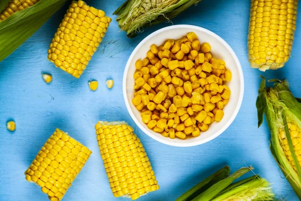 Ripe corn on a blue table close-up. Raw and canned corn in a white bowl.