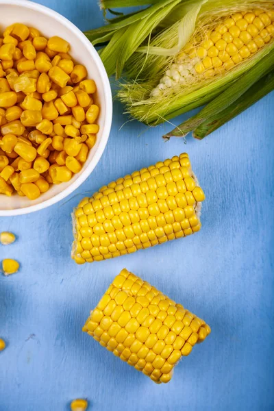 Ripe corn on a blue table close-up. Raw and canned corn in a white bowl.