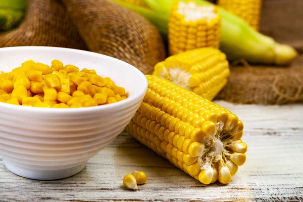 Ripe corn on a wooden table close-up. Raw and canned corn in a white bowl.
