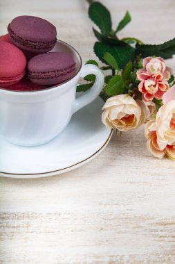 Berry macaroons beyaz Kupası ve gül ahşap arka plan üzerinde. Lezzetli kurabiye.