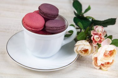 Berry macaroons beyaz Kupası ve gül ahşap arka plan üzerinde. Lezzetli kurabiye.
