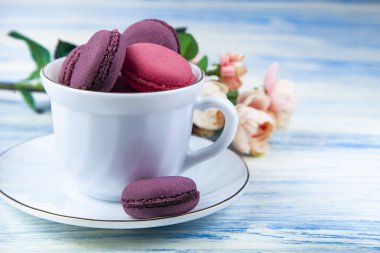 Berry macaroons beyaz Kupası ve gül mavi ahşap arka plan üzerinde. Lezzetli kurabiye.