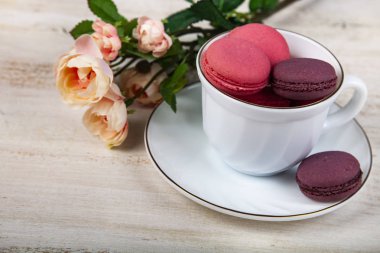 Berry macaroons beyaz Kupası ve gül ahşap arka plan üzerinde. Lezzetli kurabiye.