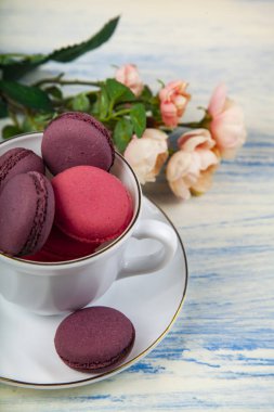 Berry macaroons beyaz Kupası ve gül mavi ahşap arka plan üzerinde. Lezzetli kurabiye.