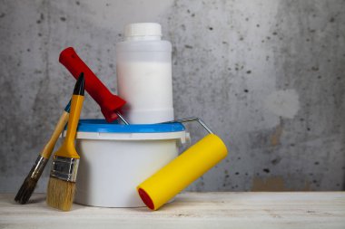 Boya, rulo ve fırça masanın üzerinde. Gri bir duvara ev ya da ofis tadilat için öğeleri.