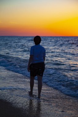 Günbatımında deniz kıyısı yürüyen genç. Aktif yaşam tarzı.
