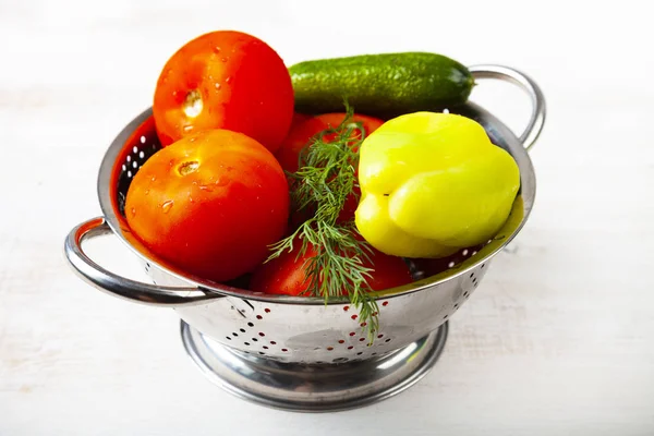 Tomatoes, peppers and cucumbers in a colander on a wooden backgr — Stock Photo, Image